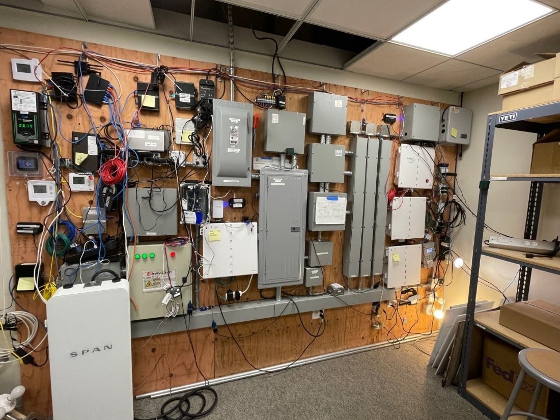 A well-organized electrical room with multiple control panels and wiring mounted on a wooden board, various labels visible.